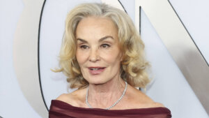 Older woman with blonde hair wearing a burgundy off-shoulder dress and diamond necklace at an event