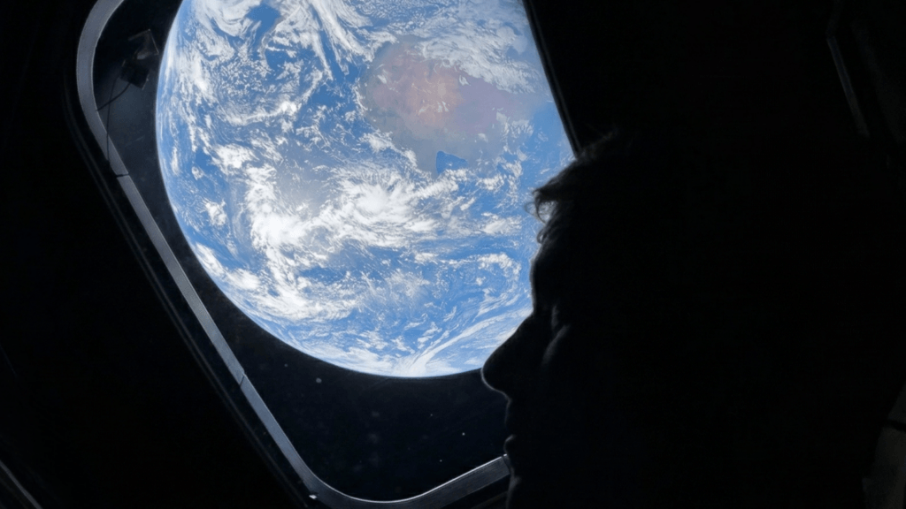Silhouette of an astronaut looking out a spacecraft window at Earth from space