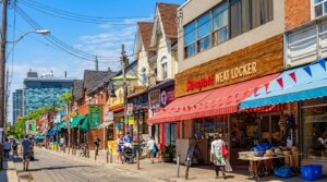Street view of people walking past shops including Springfield Meat Locker with red and blue awnings on a sunny day