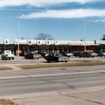 Vintage Walmart Discount City storefront with classic cars in parking lot and adjacent IGA Supermarket and A&W signs