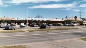 Vintage Walmart Discount City storefront with classic cars in parking lot and adjacent IGA Supermarket and A&W signs
