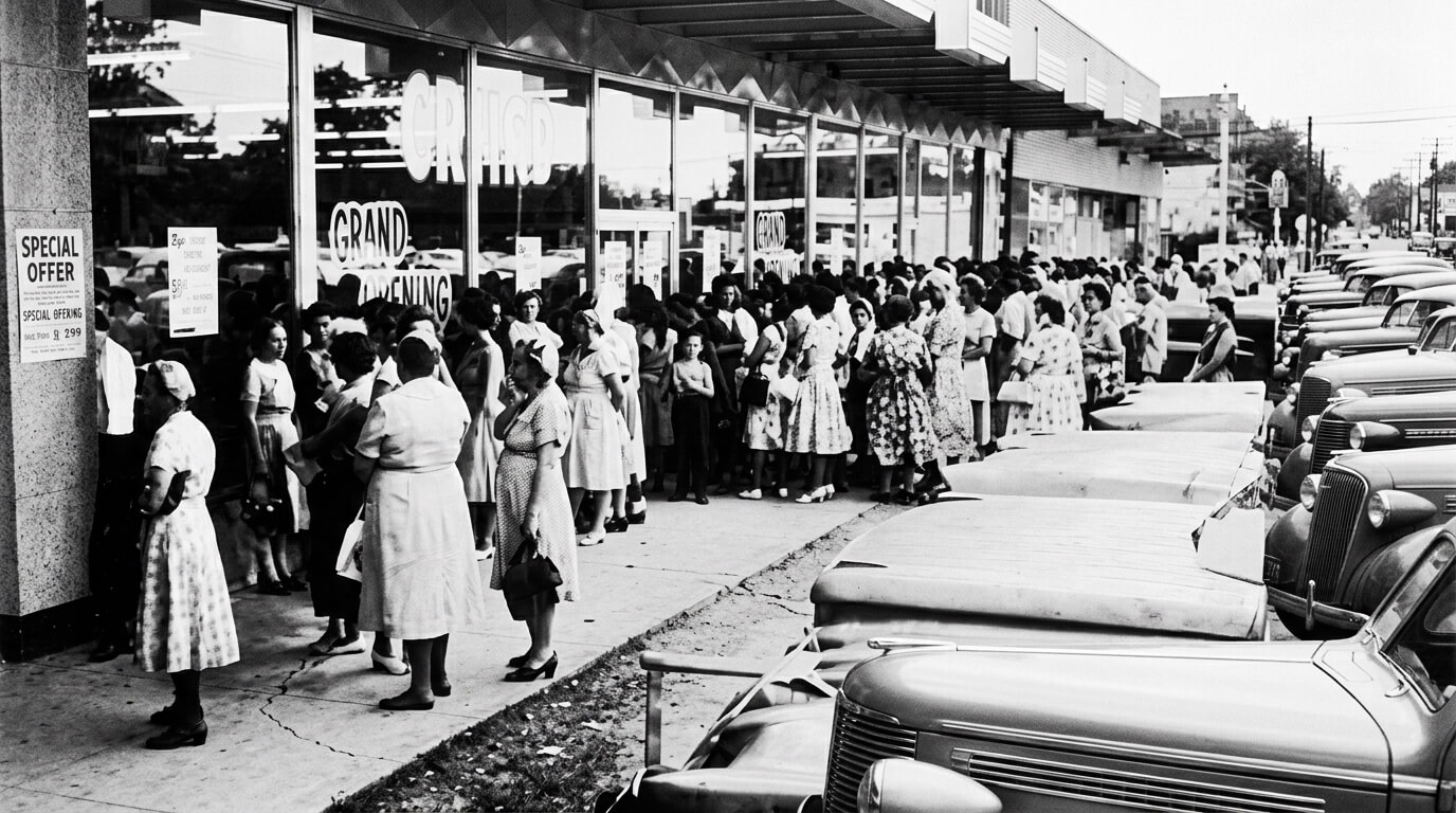 Crowd of women lined up outside a store for a grand opening event in the mid-20th century.