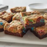 Brownie blondie bars with colorful candy pieces on a white serving platter with stacked plates in the background