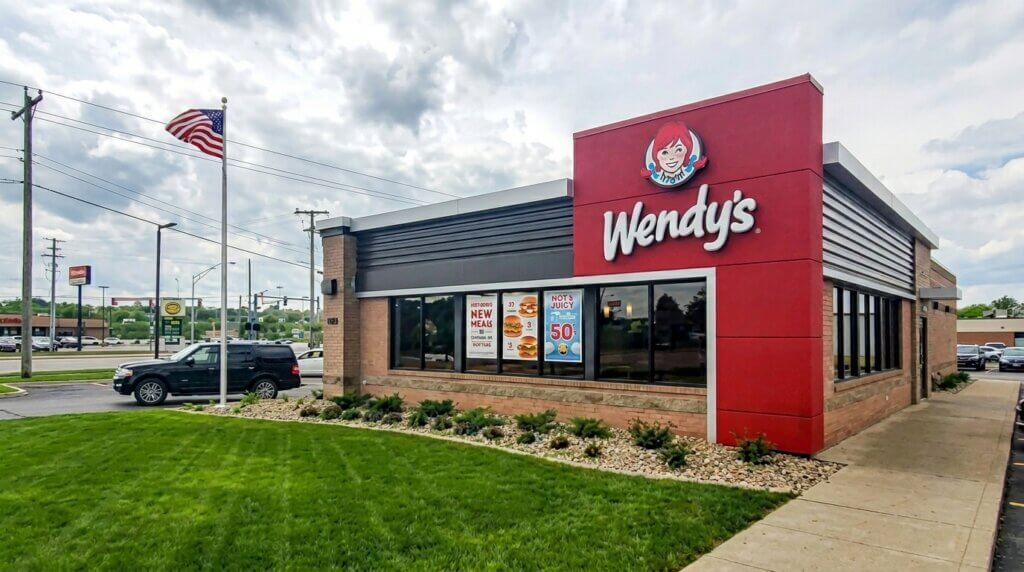 Wendy's fast food restaurant exterior with American flag and promotional posters on windows.