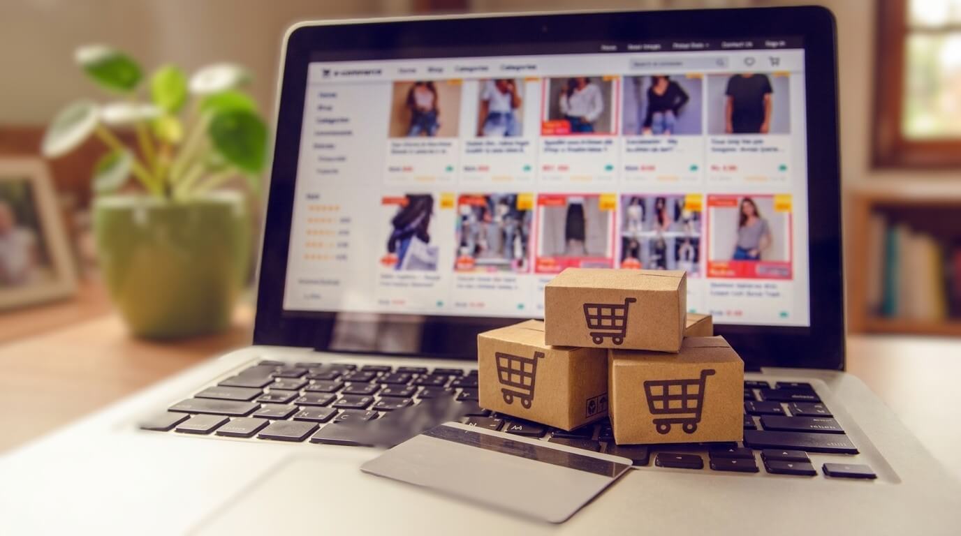 Laptop displaying online shopping site with small cardboard boxes and a credit card on the keyboard