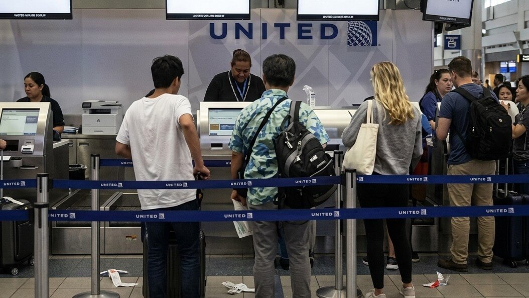 Passengers waiting in line at United Airlines check-in counters in an airport terminal.