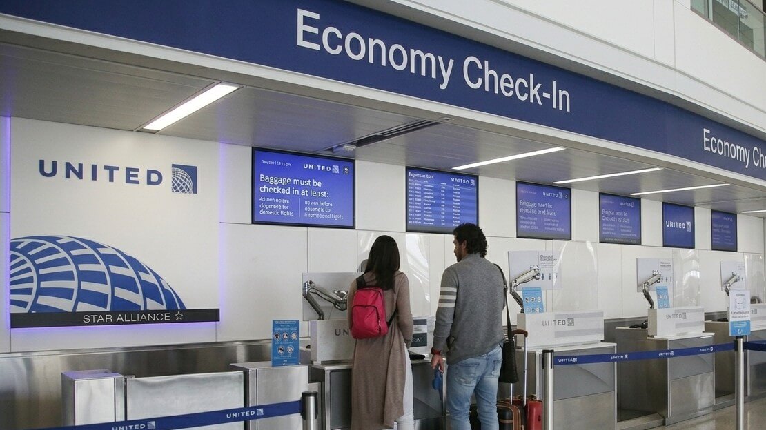 Two travelers checking in at United Airlines economy check-in counters at an airport.