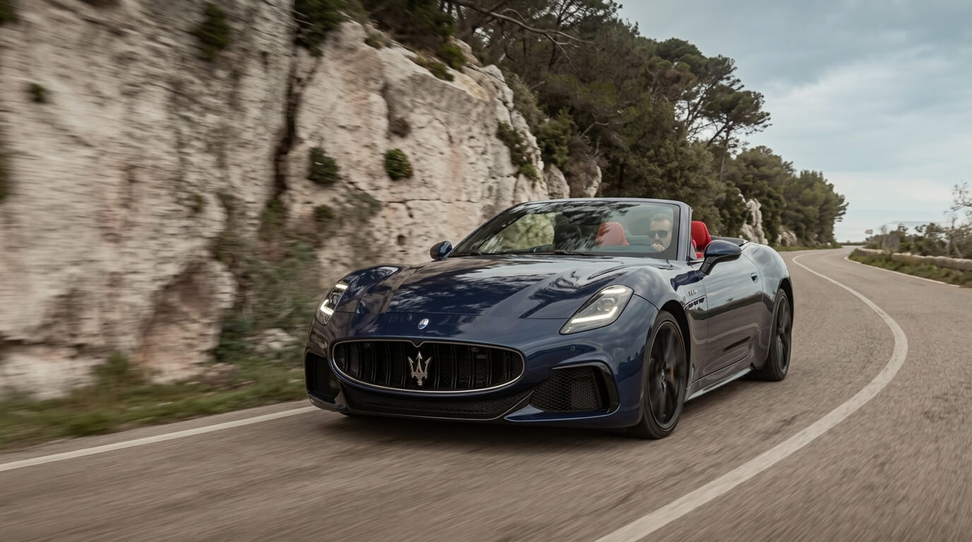 Blue Maserati convertible with red interior driving on a winding road near rocky cliffs and trees