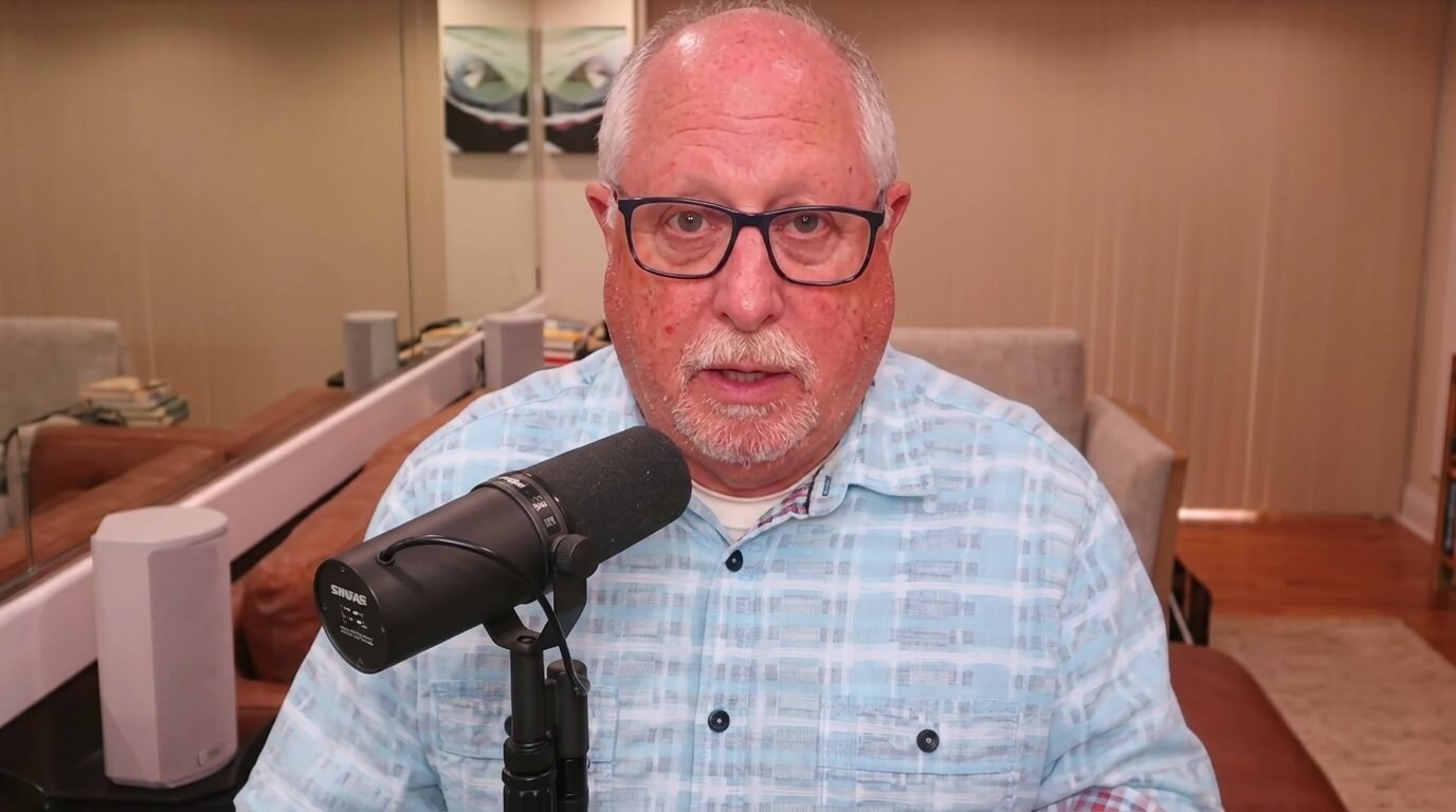 Older man with glasses speaking into a Shure microphone in a home recording setup