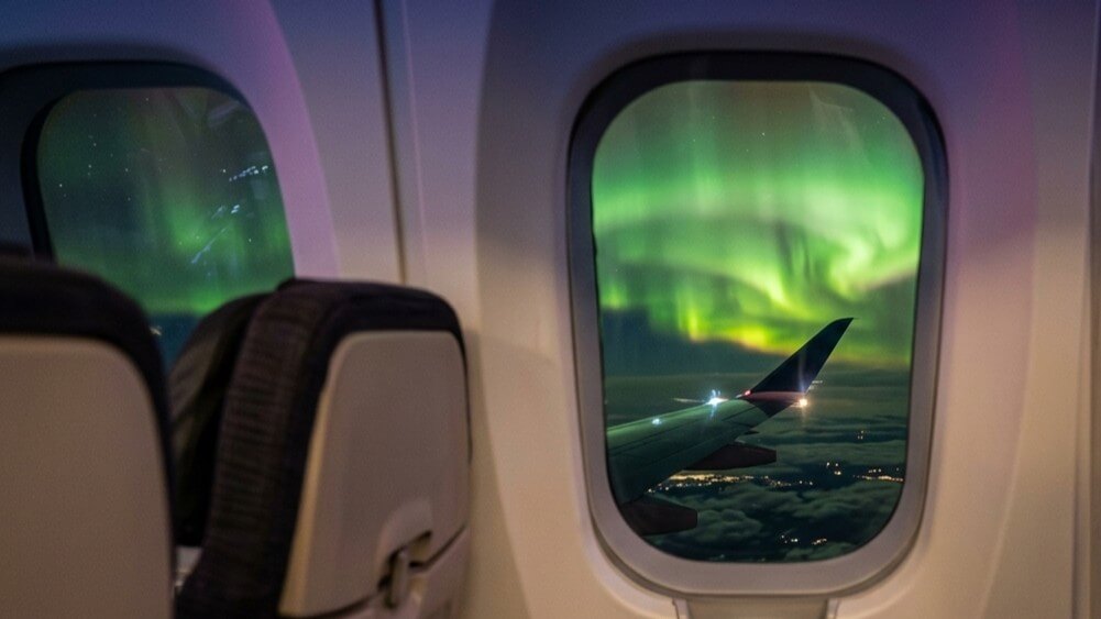 Northern lights visible through an airplane window above clouds at night.