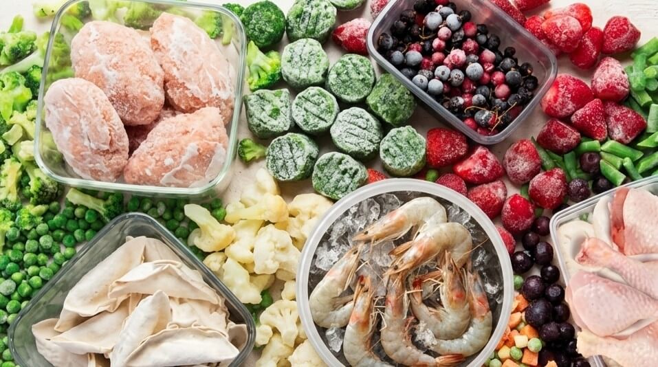 Frozen vegetables, berries, shrimp, dumplings, and chicken drumsticks arranged in containers and loose on a surface.