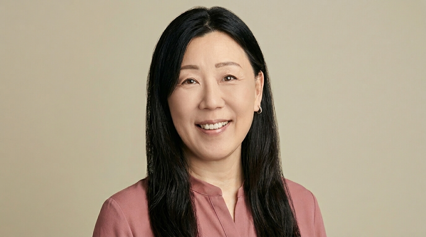 Asian woman with long black hair wearing a mauve blouse smiling against a beige background