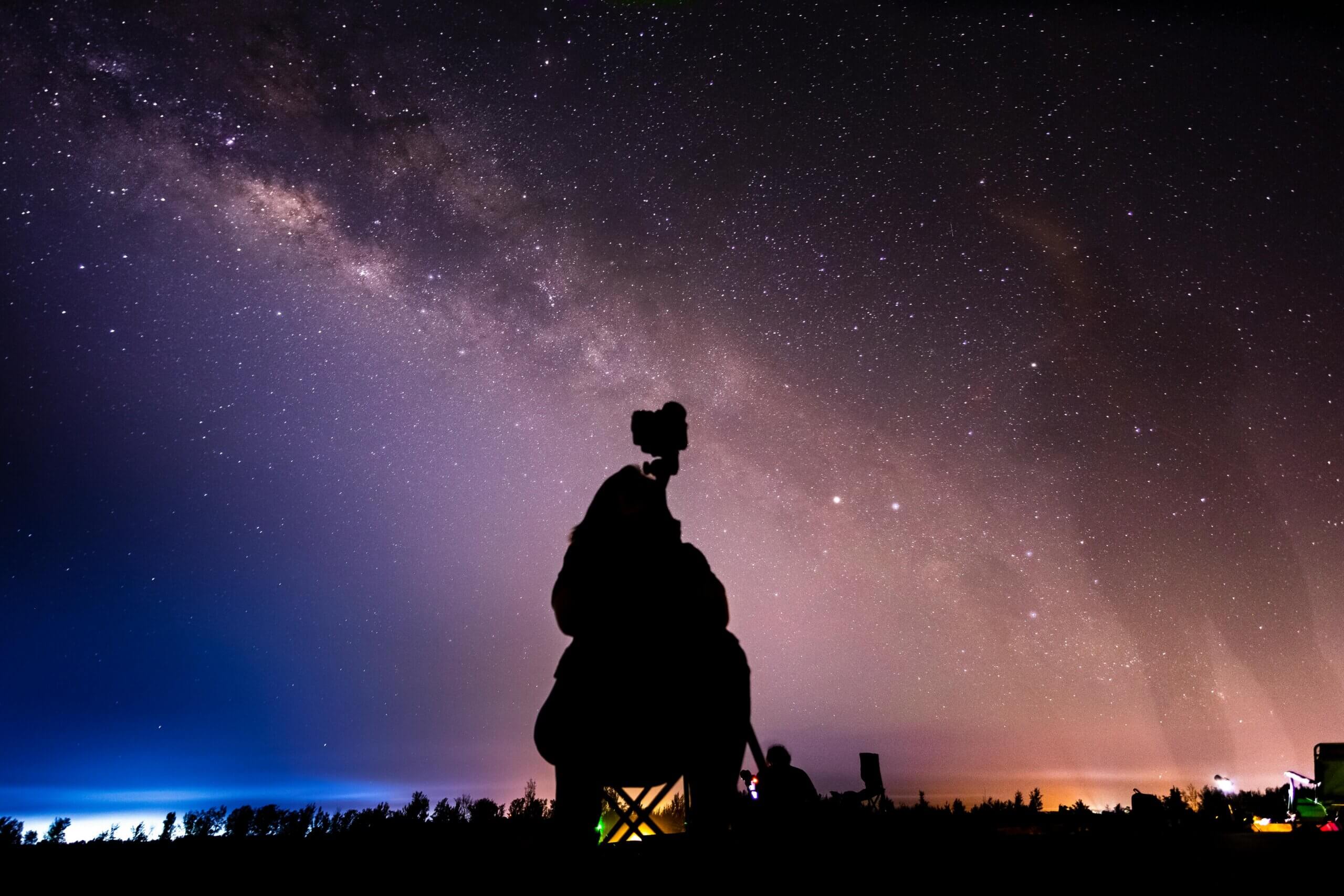 Silhouette of a person photographing the Milky Way galaxy under a starry night sky.