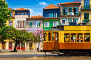 Yellow vintage tram passing colorful residential buildings with tiled facades in a sunny urban setting.