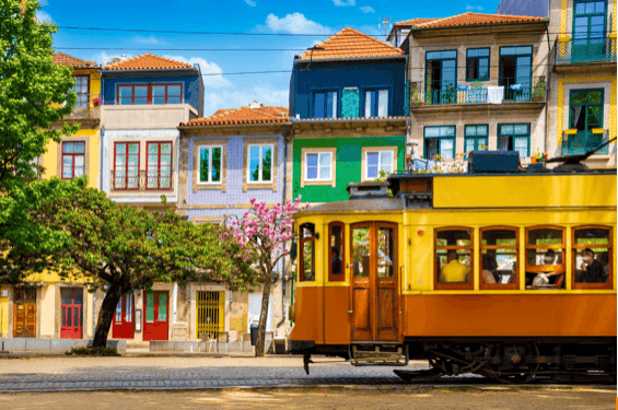 Yellow vintage tram passing colorful residential buildings with tiled facades in a sunny urban setting.