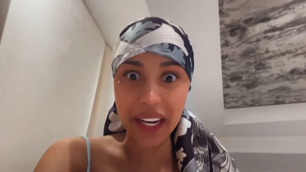 Woman wearing a black and white floral headscarf speaking with wide eyes in a room with white walls and abstract art
