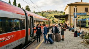 Train conductor greeting passengers boarding the Frecciarossa train at Val d'Orcia Castello station in Italy.