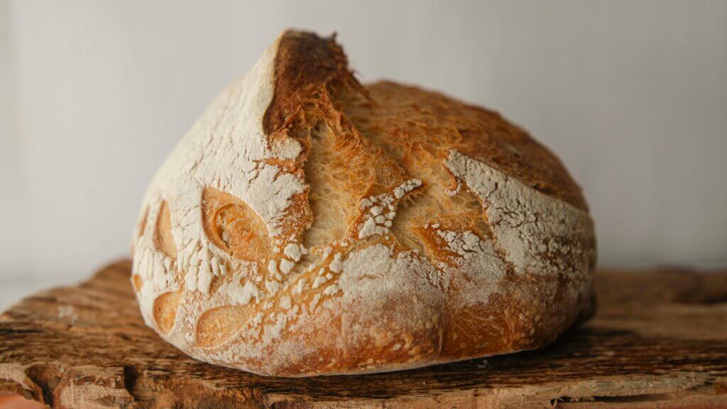 Round loaf of rustic sourdough bread with a cracked crust on a wooden surface
