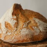 Round loaf of rustic sourdough bread with a cracked crust on a wooden surface