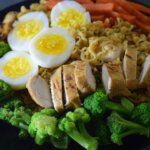 Plate with sliced grilled chicken, hard-boiled eggs, broccoli, carrots, mushrooms, and noodles