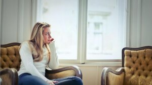 Young woman in a white sweater sitting on a vintage armchair looking out a bright window