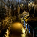 Illuminated walkway inside a cave with stalactites hanging from the ceiling and water on the side