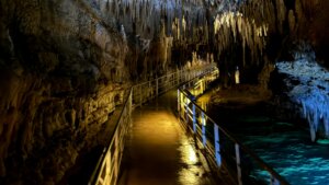 Illuminated walkway inside a cave with stalactites hanging from the ceiling and water on the side