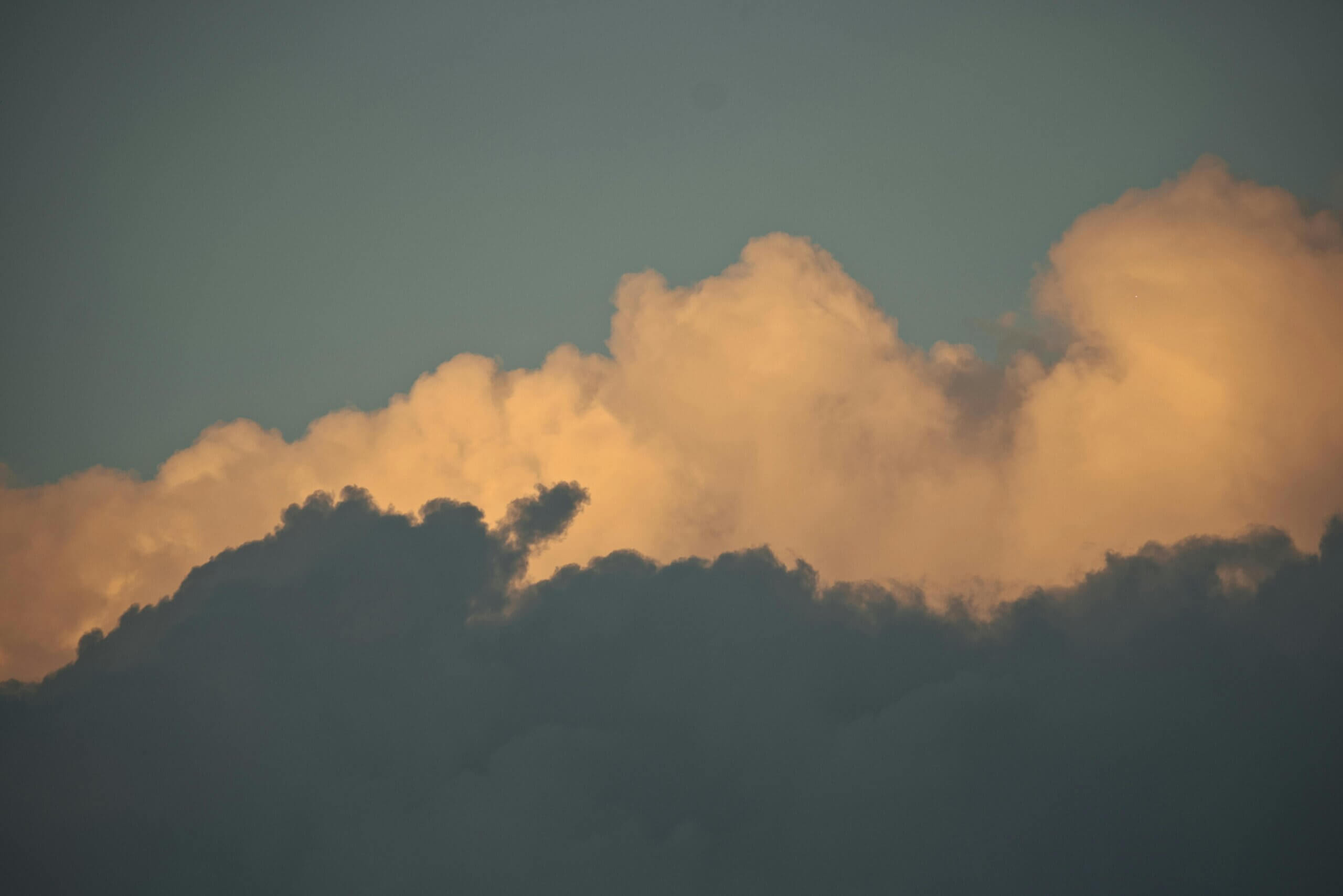Dark clouds with golden sunlight illuminating the upper edges against a clear sky.