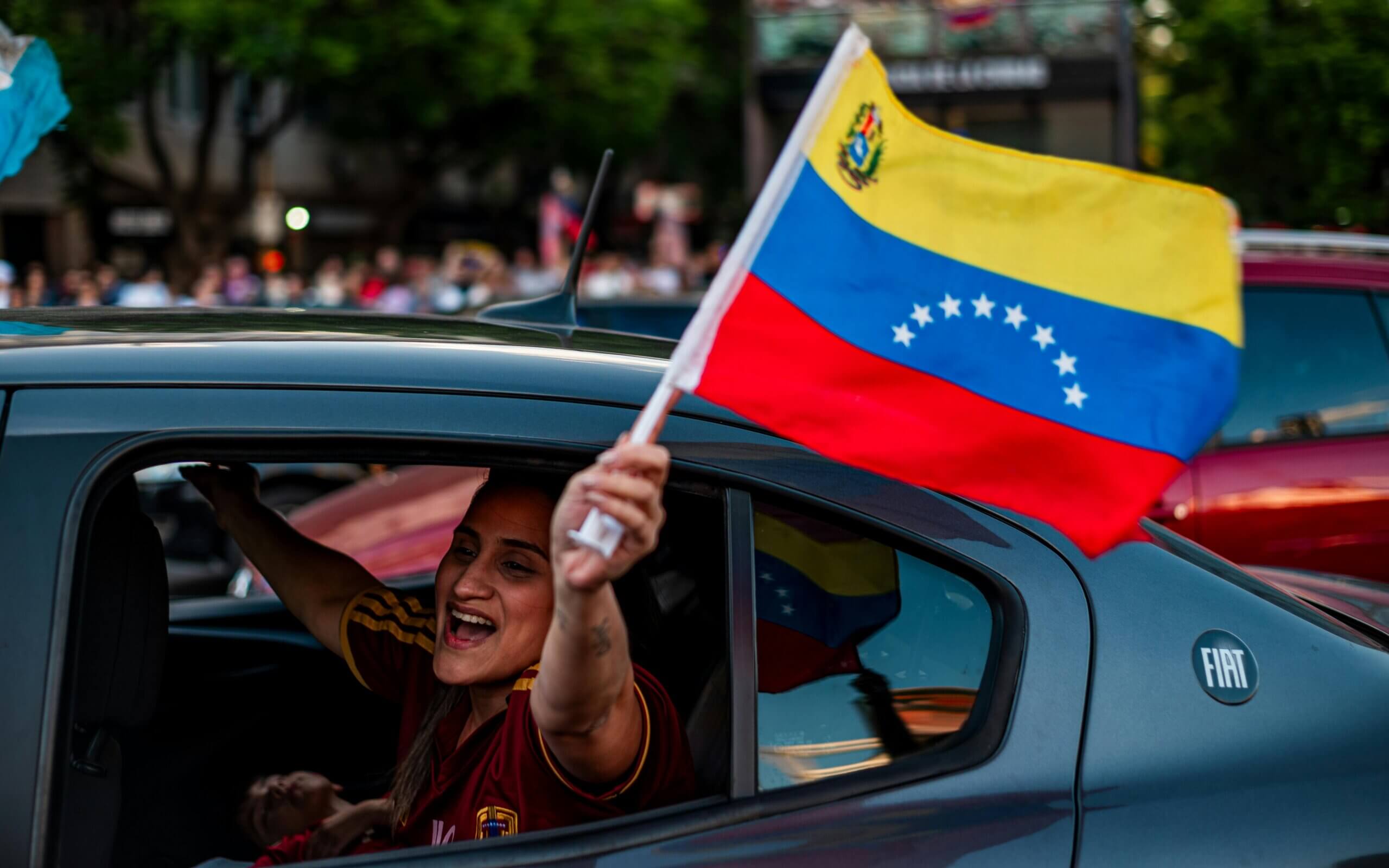 Woman waving Venezuelan flag from a black Fiat car window during a street celebration