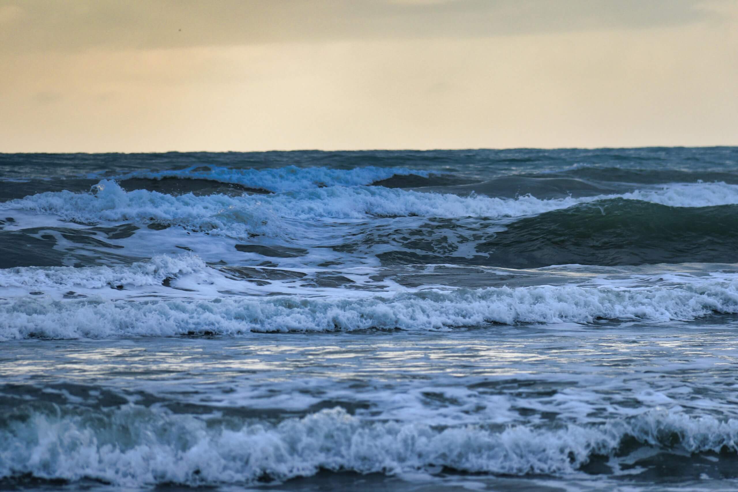 Ocean waves crashing under a cloudy sky at sunset.