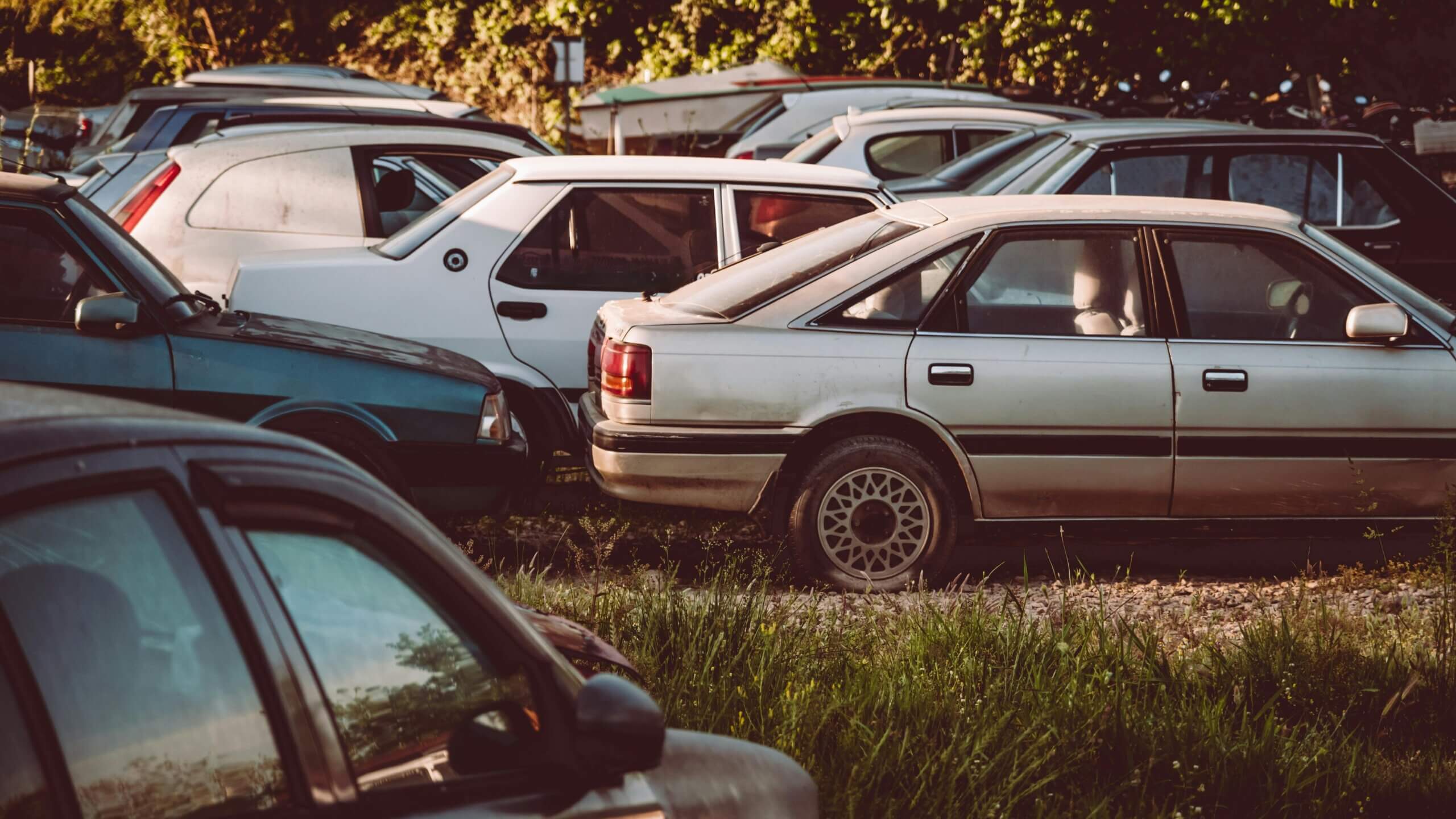 Several older model cars parked closely together in a grassy lot during sunset.