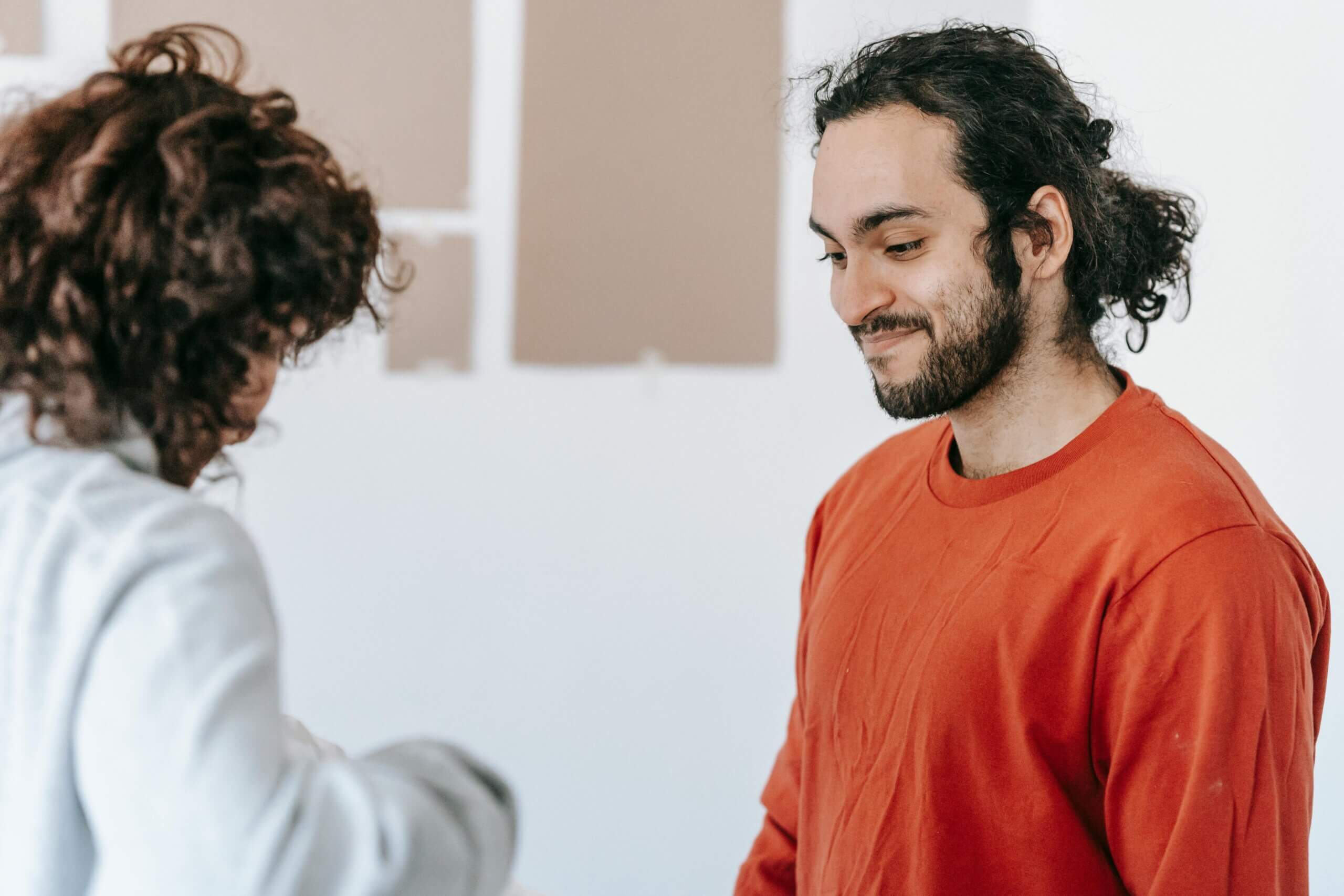 Man with curly hair and beard wearing a red shirt smiling at a person with curly hair in a gray sweater