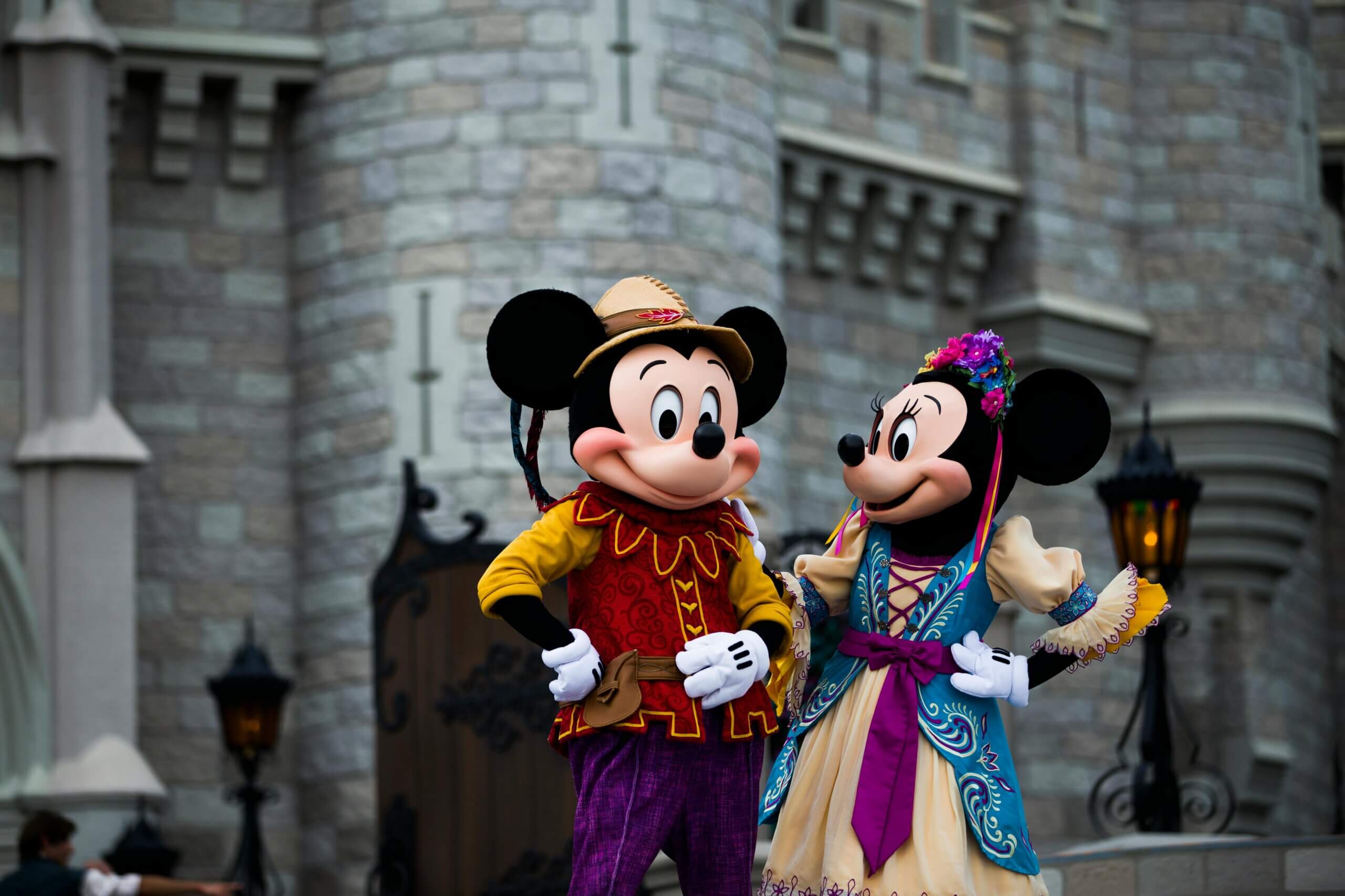 Mickey Mouse and Minnie Mouse in colorful medieval-style costumes posing in front of a castle wall.