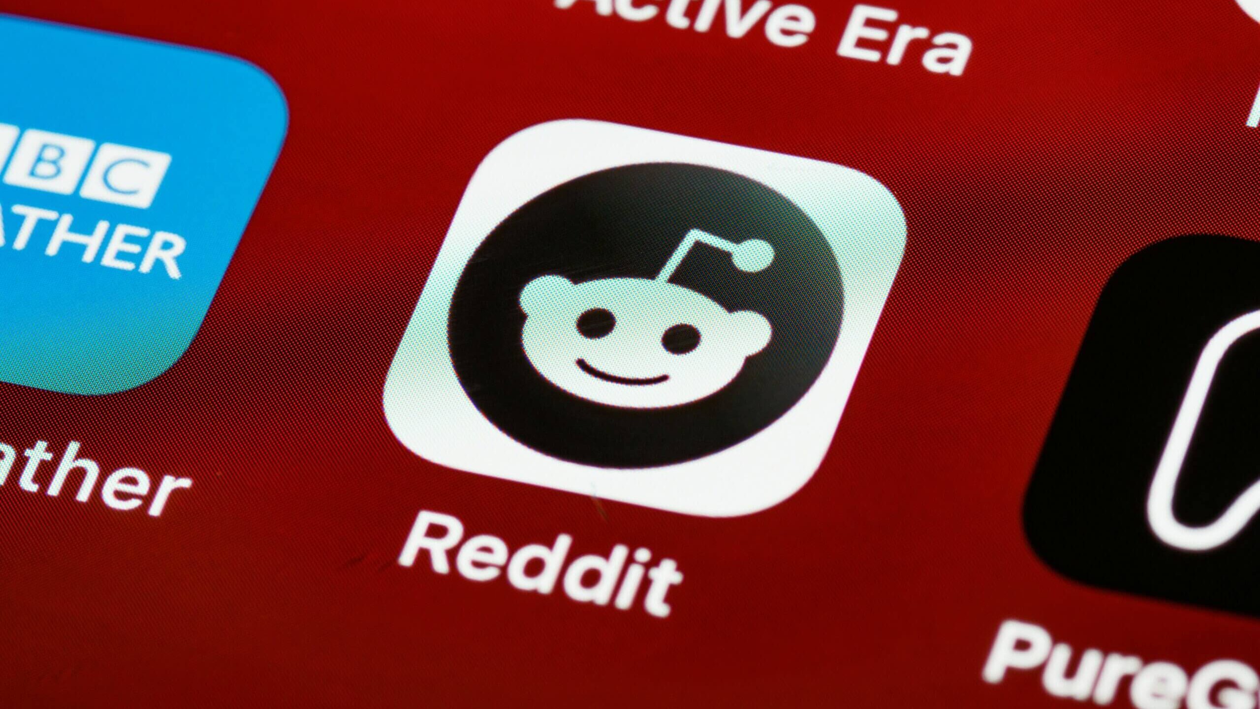 Reddit app icon with a black and white smiling alien logo on a red smartphone screen.