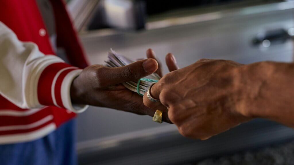 Two people exchanging a thick stack of cash held together by a rubber band