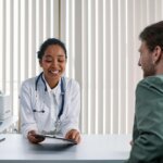 Smiling female doctor with stethoscope showing tablet to male patient in medical office