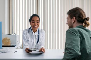 Smiling female doctor with stethoscope showing tablet to male patient in medical office