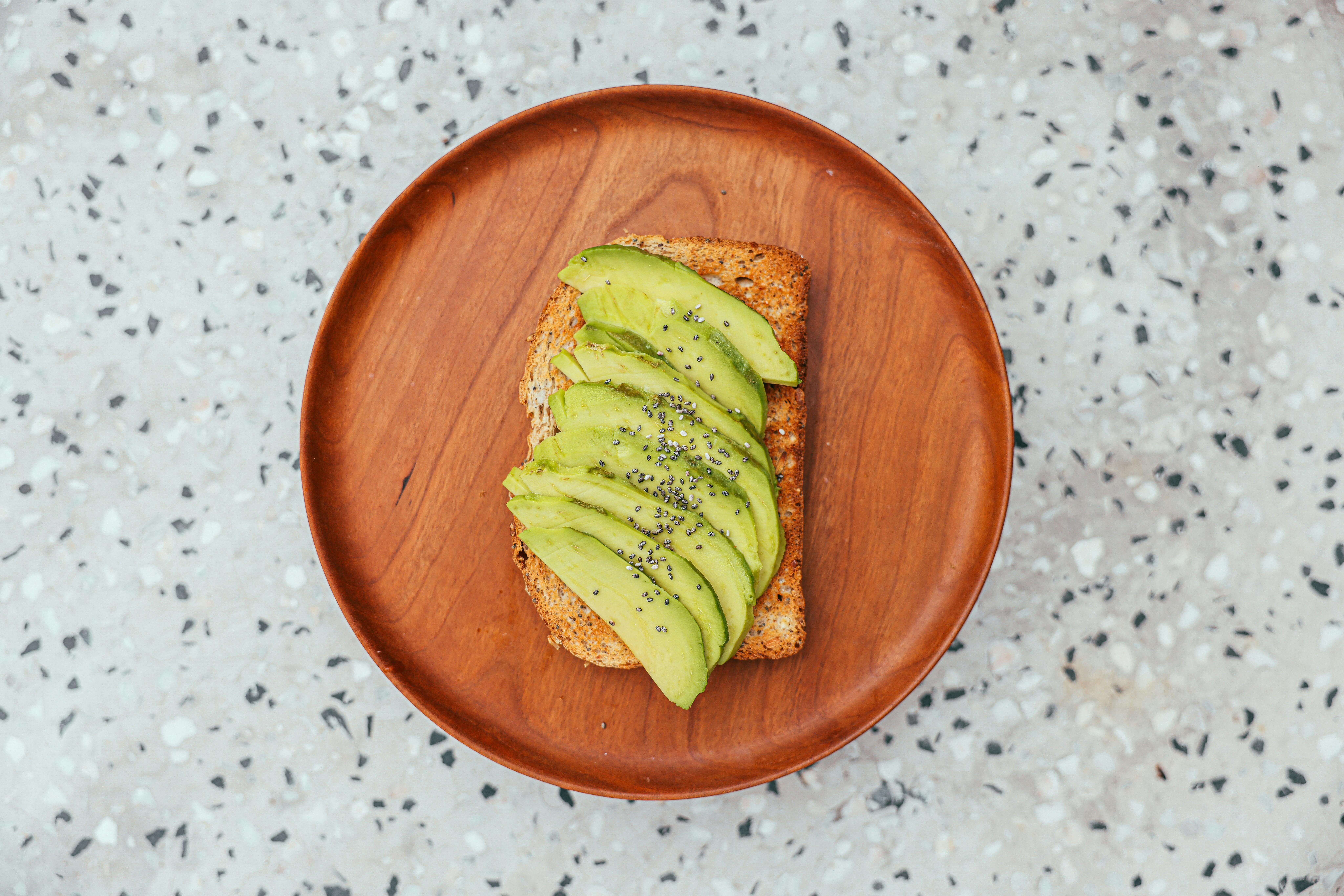 Sliced avocado with chia seeds on toasted whole grain bread on a wooden plate
