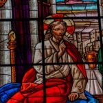 Stained glass window depicting Jesus with a halo and red robe, seated beside a man in green holding a scroll.