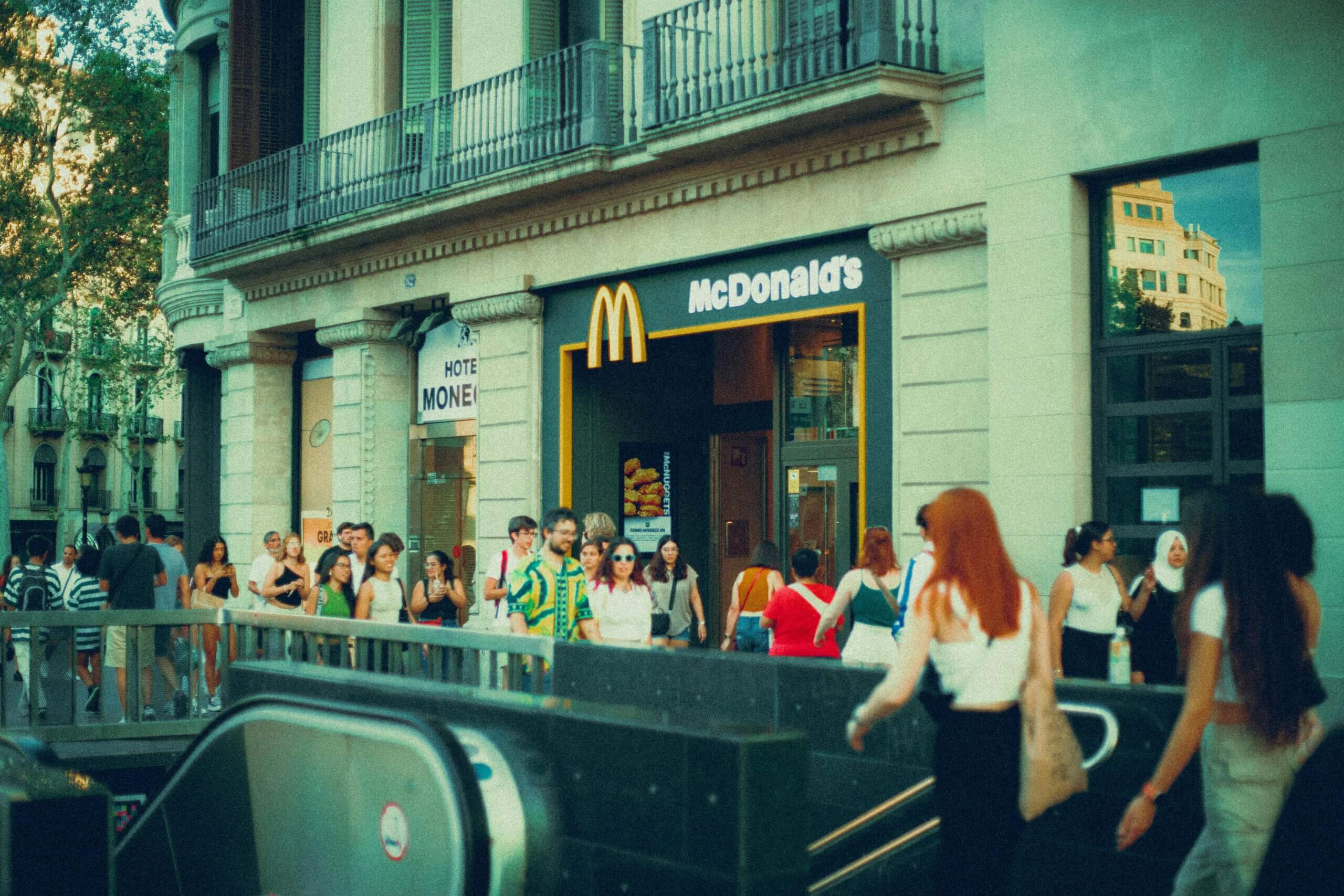 Crowd of people walking past a McDonald's restaurant entrance on a city street.
