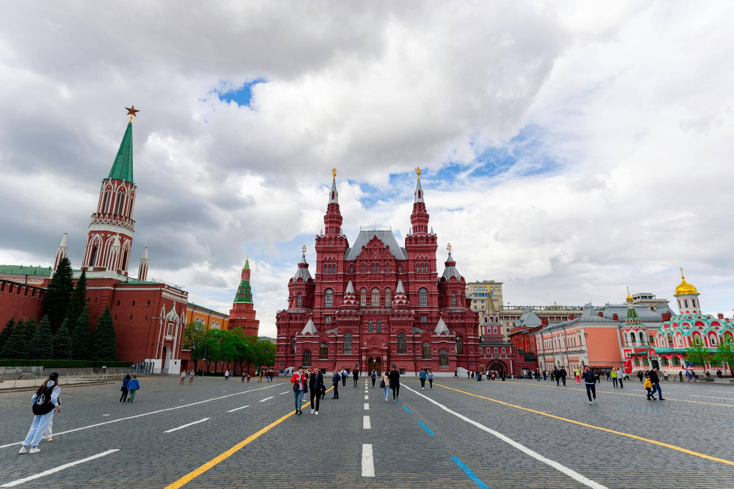 People walking in Red Square with the State Historical Museum and Kremlin towers in Moscow, Russia under a cloudy sky