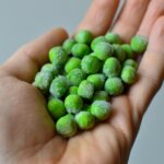 Hand holding frozen green peas with visible ice crystals against a gray background