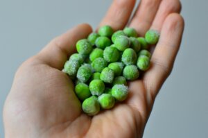 Hand holding frozen green peas with visible ice crystals against a gray background