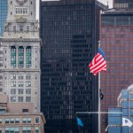 American flag and other flags flying in front of Boston's Custom House Tower and surrounding skyscrapers