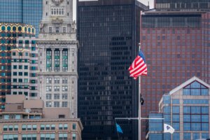 American flag and other flags flying in front of Boston's Custom House Tower and surrounding skyscrapers