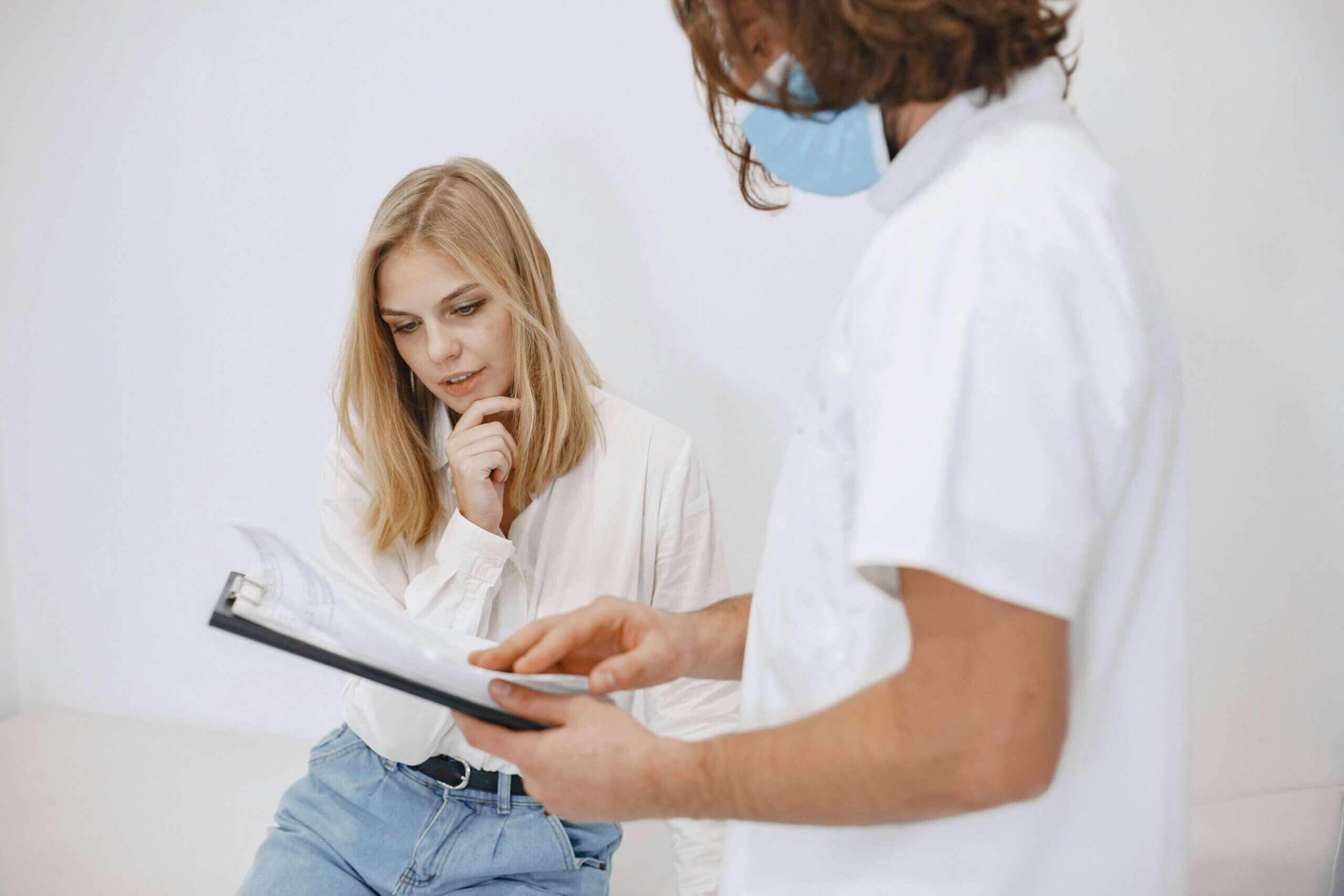 Woman in white shirt and jeans reviewing documents with masked healthcare professional in white coat
