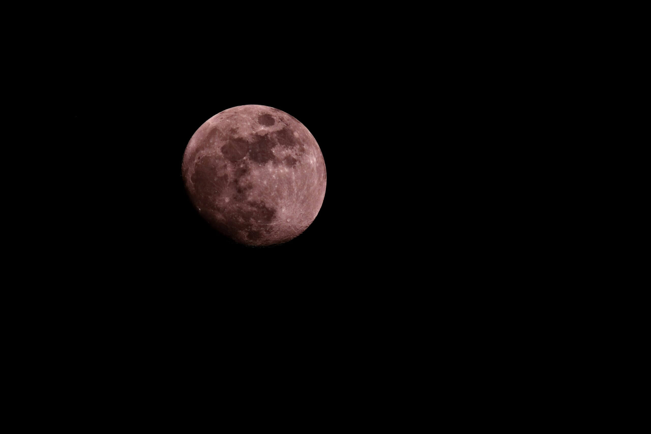 Close-up of a reddish full moon against a black night sky
