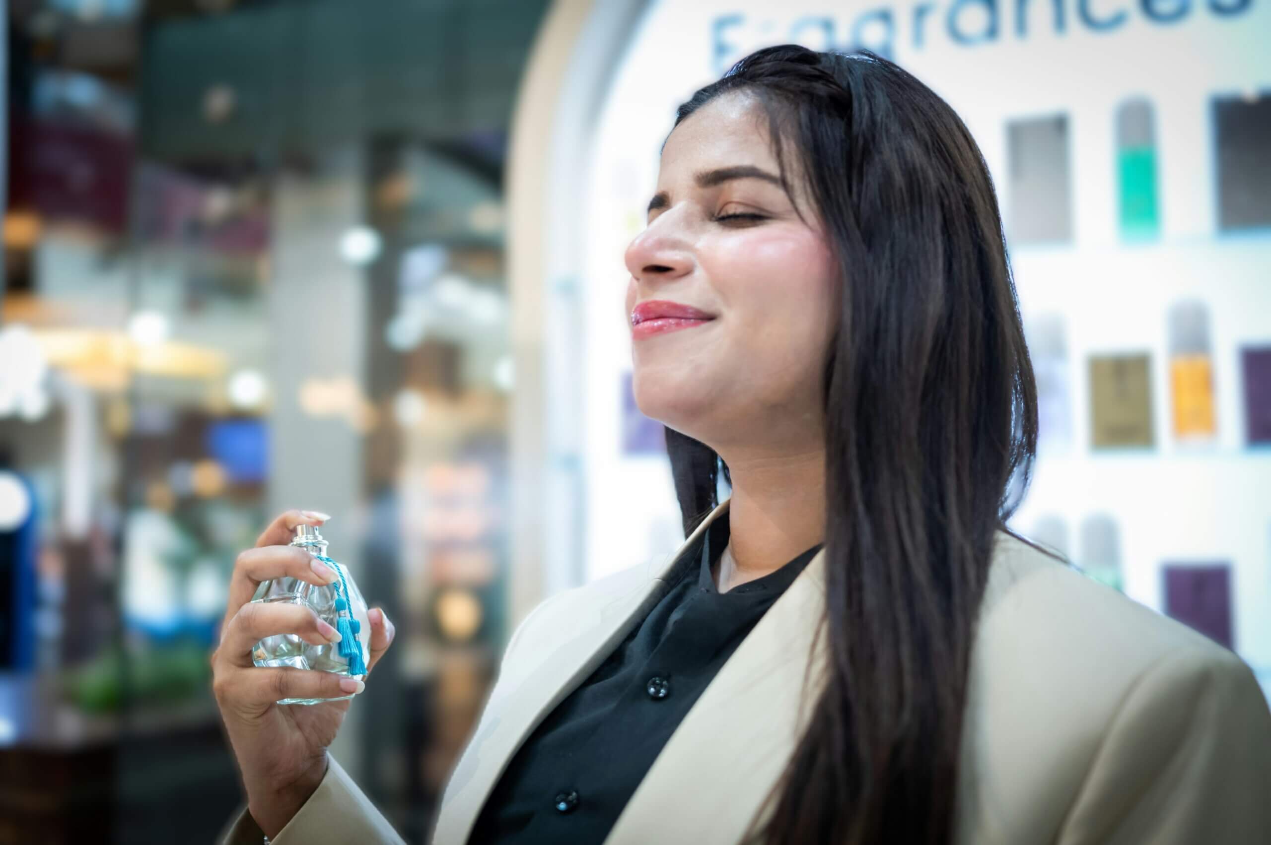 Woman with long dark hair spraying perfume with eyes closed in a fragrance store