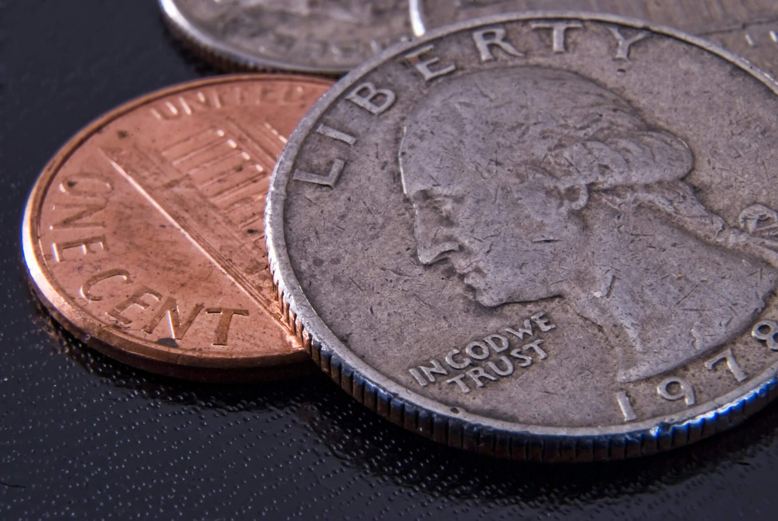 Close-up of a 1978 US quarter and a US one-cent penny on a black surface.