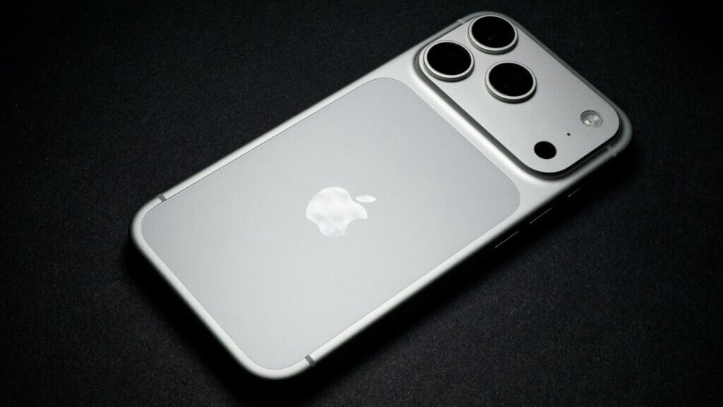 Silver Apple iPhone with triple camera lenses on a black surface